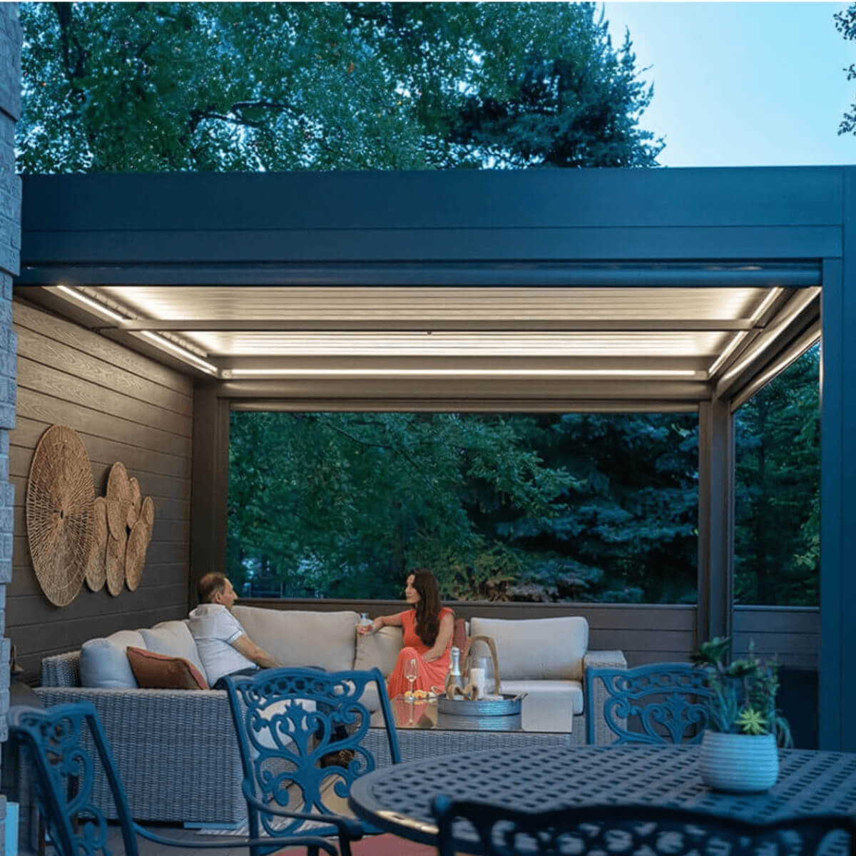 Covered outdoor living area under a black pergola with ambient lighting and comfortable seating.