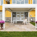 White freestanding aluminum pergola creating a covered patio seating space in front of a yellow house.