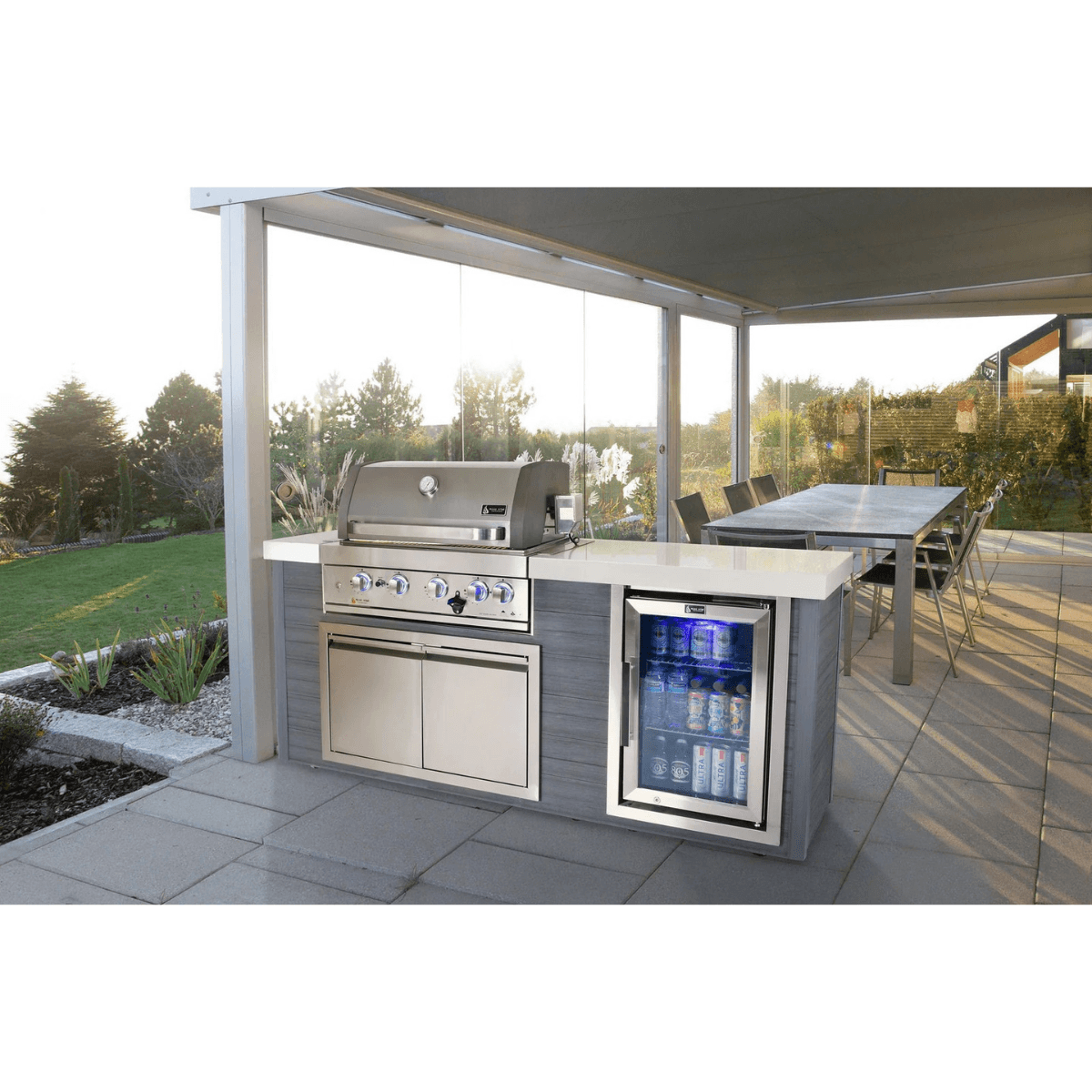 Mont Alpi 4-Burner Stainless Steel Art-wood Outdoor Island Grill installed in a covered outdoor dining area with modern patio seating and built-in refrigeration.