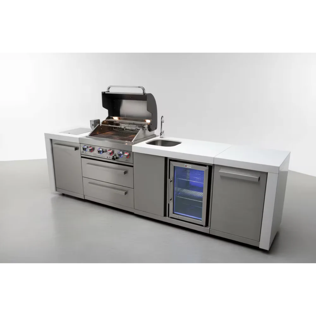 Angled view of the Mont Alpi 400 Deluxe Island with the grill hood open, highlighting the cooking area, sink, beverage centre fridge, and stainless steel storage cabinets.