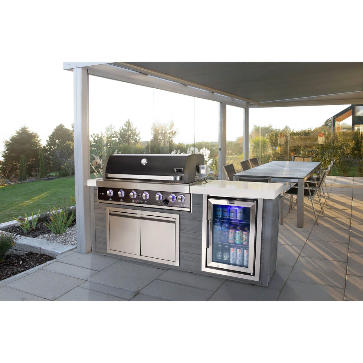 Mont Alpi 6-Burner Black Stainless Steel Art-wood Outdoor Island Grill installed in a covered patio dining area with illuminated beverage fridge and modern outdoor entertaining space.