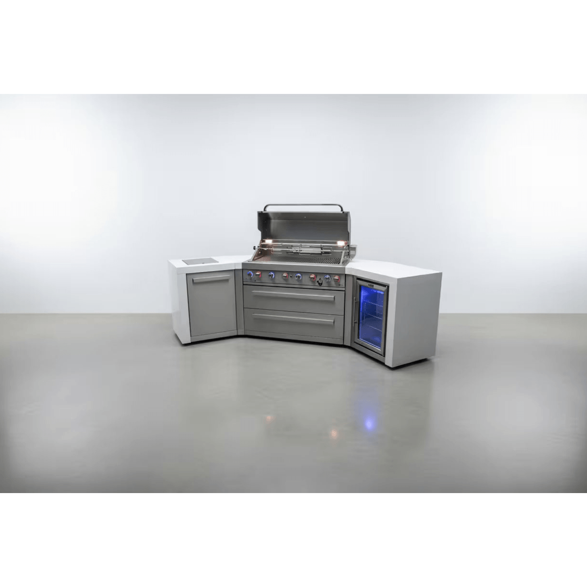 Front view of the Mont Alpi 805 Deluxe Island with 45-degree corners, featuring an open gas grill, double storage drawers, side cabinet, and integrated outdoor fridge with blue interior lighting.