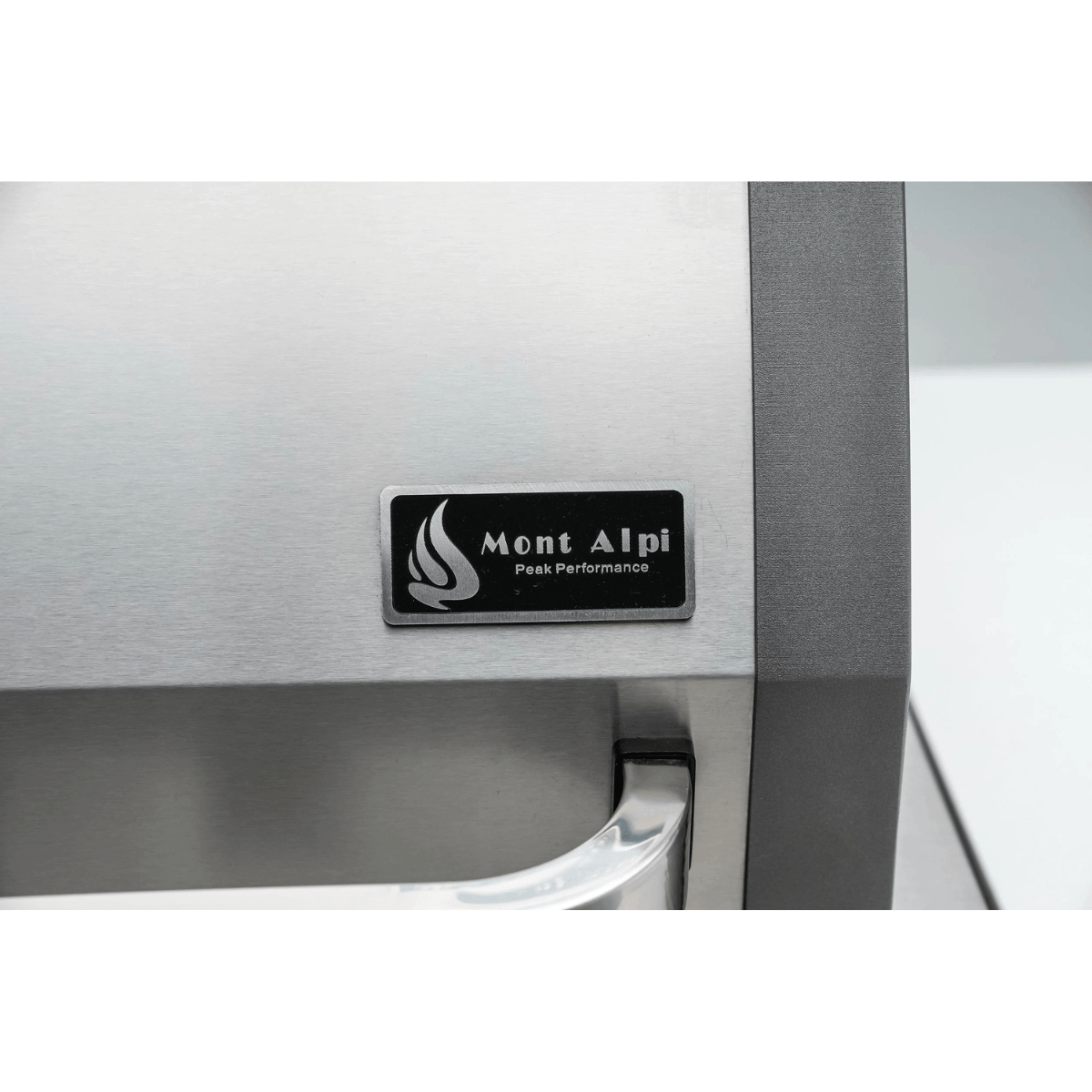 Close-up of the Mont Alpi logo badge mounted on the stainless steel grill hood, showcasing the brand’s premium finish and craftsmanship.