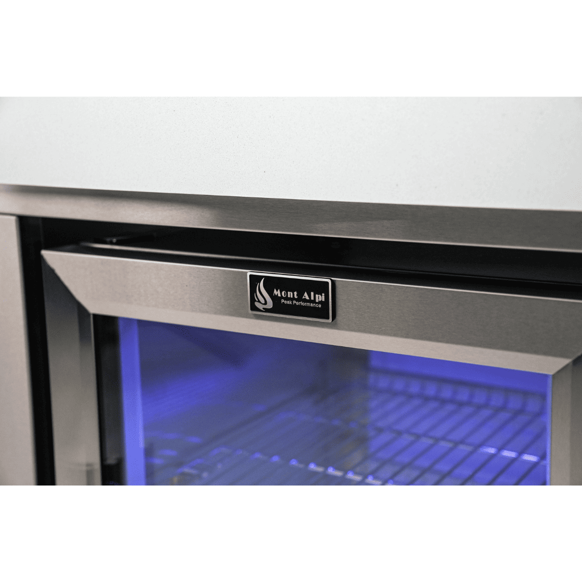 Mont Alpi logo displayed on the black stainless steel fridge cabinet door with blue LED interior lighting visible through the glass.