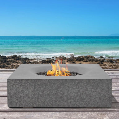 Pyromania Monument concrete fire table with flames on an outdoor beachfront deck.