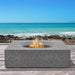 Pyromania Monument concrete fire table with flames on an outdoor beachfront deck.
