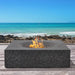 Dark grey Pyromania Monument fire table with active flames overlooking the ocean.