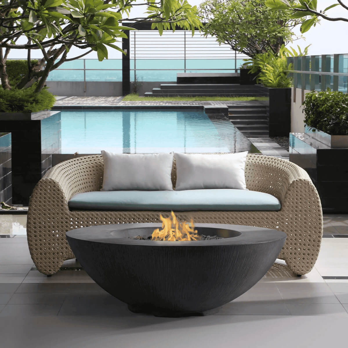 Dark grey Pyromania Shangri-La fire table with flames beside a luxury poolside seating area.