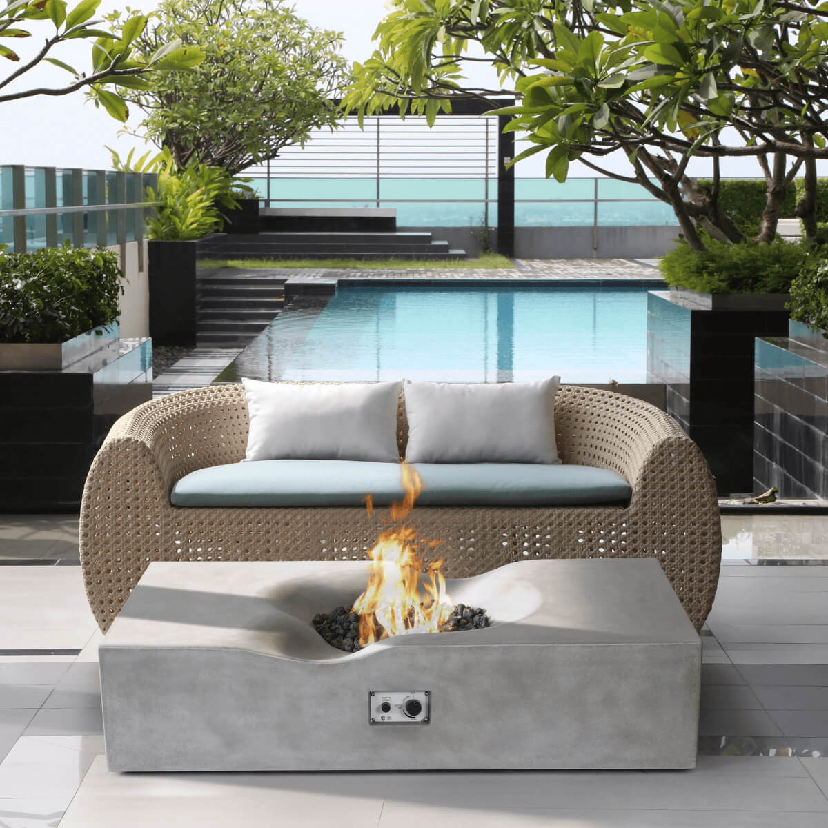 Light grey Pyromania Venice fire table with active flame beside a woven outdoor sofa.